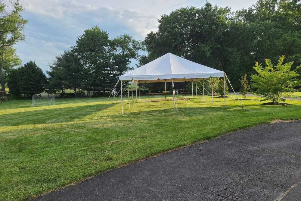 A white frame tent set up on an open lawn with trees behind it