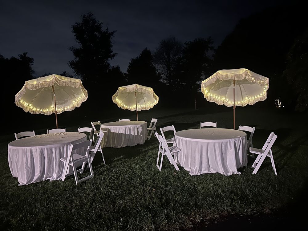 Fairy lights glowing along the ribs of white umbrellas over dressed tables at night